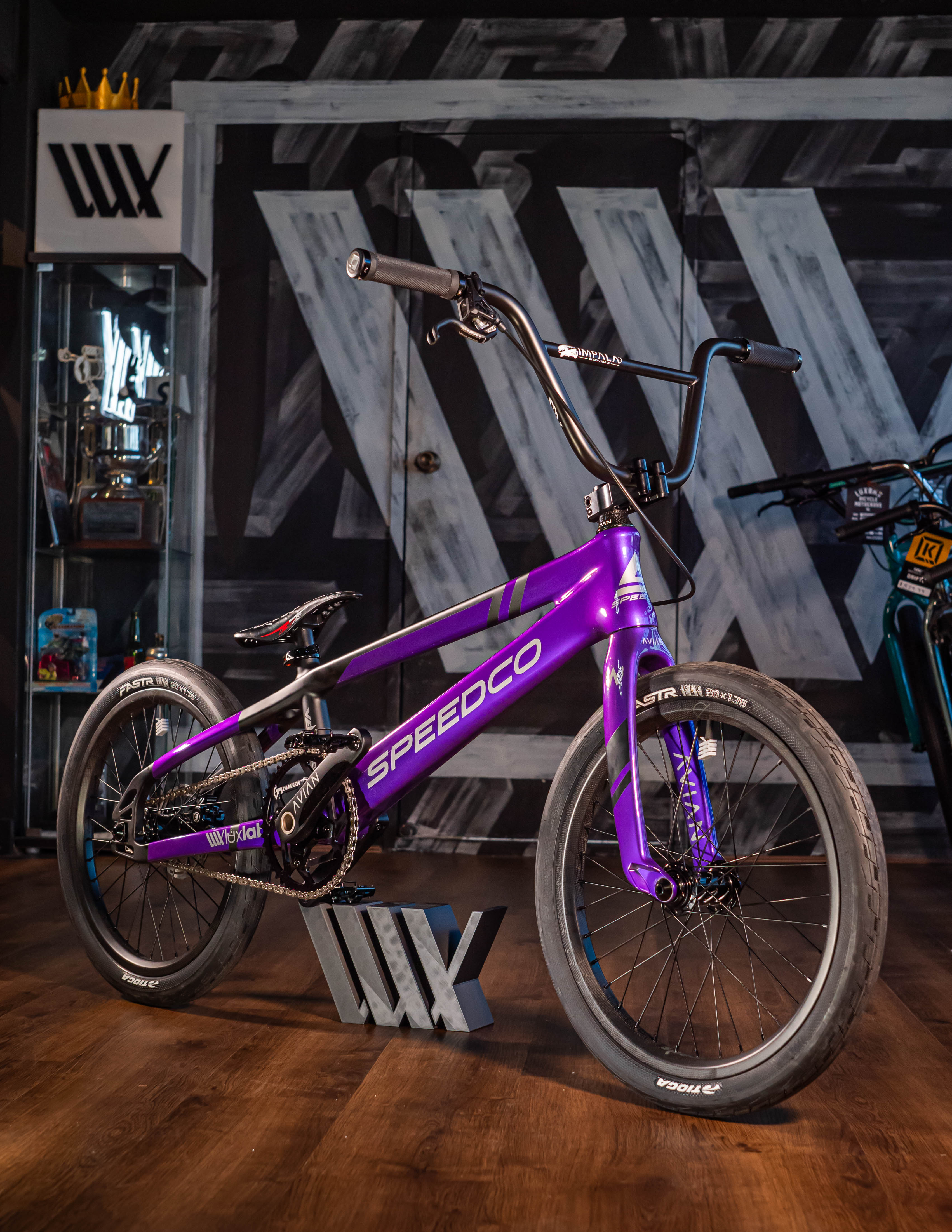 Purple BMX bike displayed indoors on a wooden floor with geometric patterns in the background.