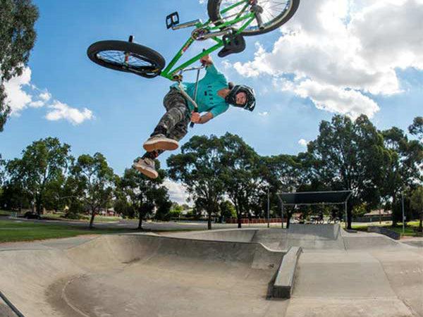 A bmx rider performing an inverted trick above a concrete skatepark bowl under a clear sky.