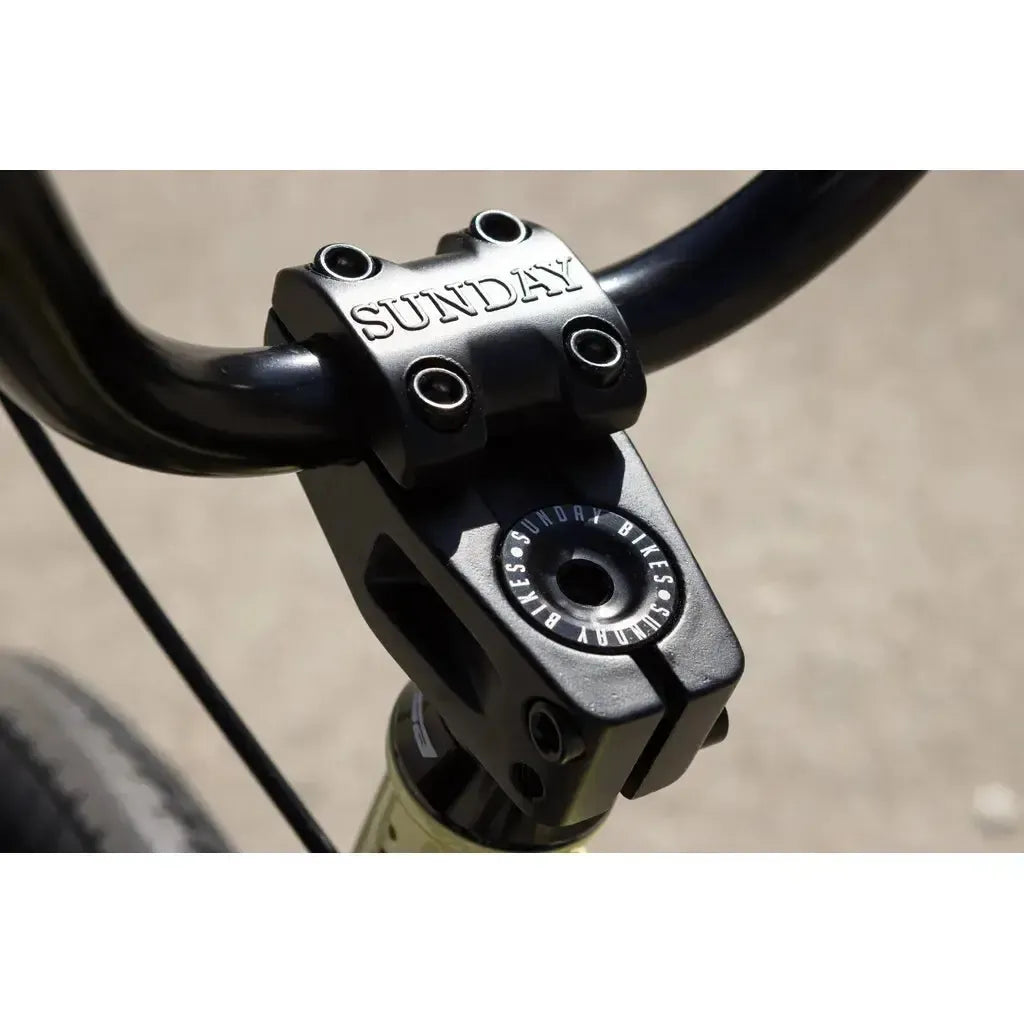 Close-up of a black BMX stem and handlebars with "SUNDAY" engraved on the stem and "SUNDAY BIKES" on the cap, showcasing Odyssey parts featured on the 2025 Sunday Soundwave Special Bike.