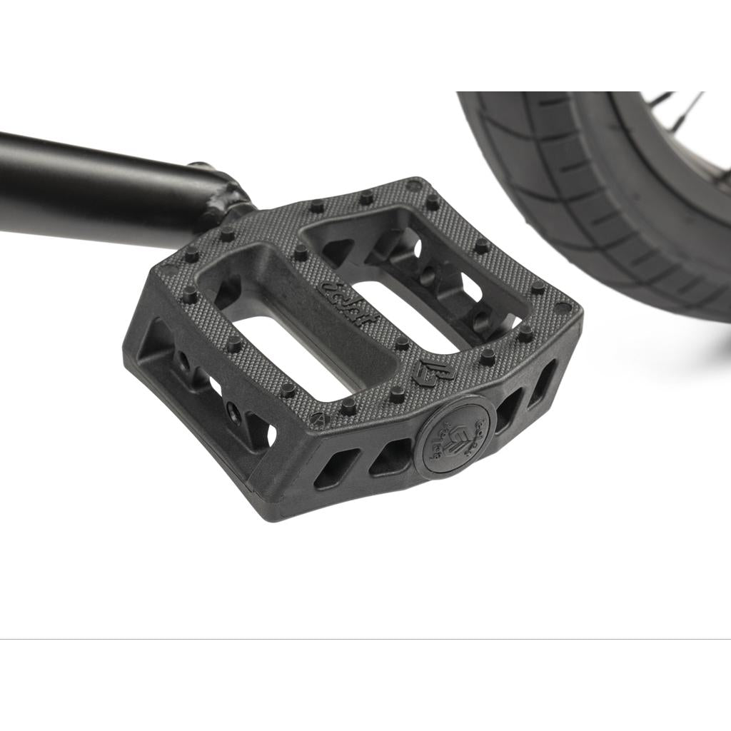 Close-up of a black pedal attached to the crank arm of a Wethepeople CRS FC 20 Inch Bike, with part of the tire visible in the background.