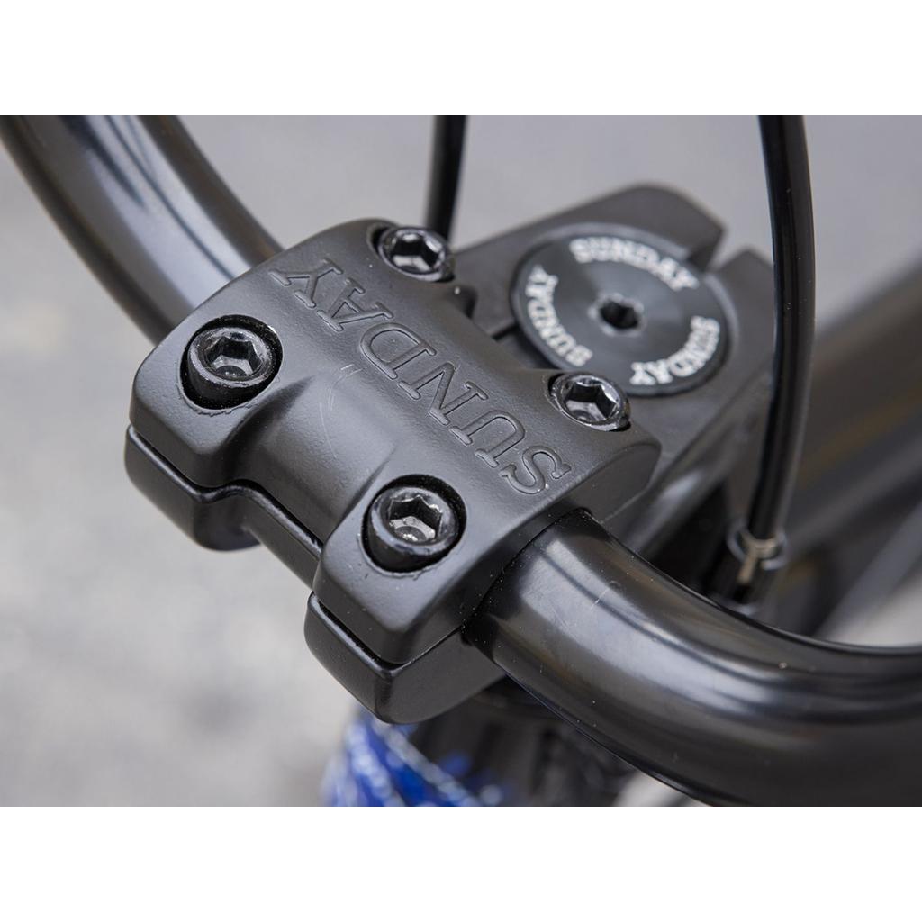 Close-up of the black handlebar stem with "SUNDAY" engraved on the front plate and visible bolts, shown on the Sunday Forecaster Maca Grasset 20 Inch Bike—perfect for BMX riders seeking precision in park or gyro setups.