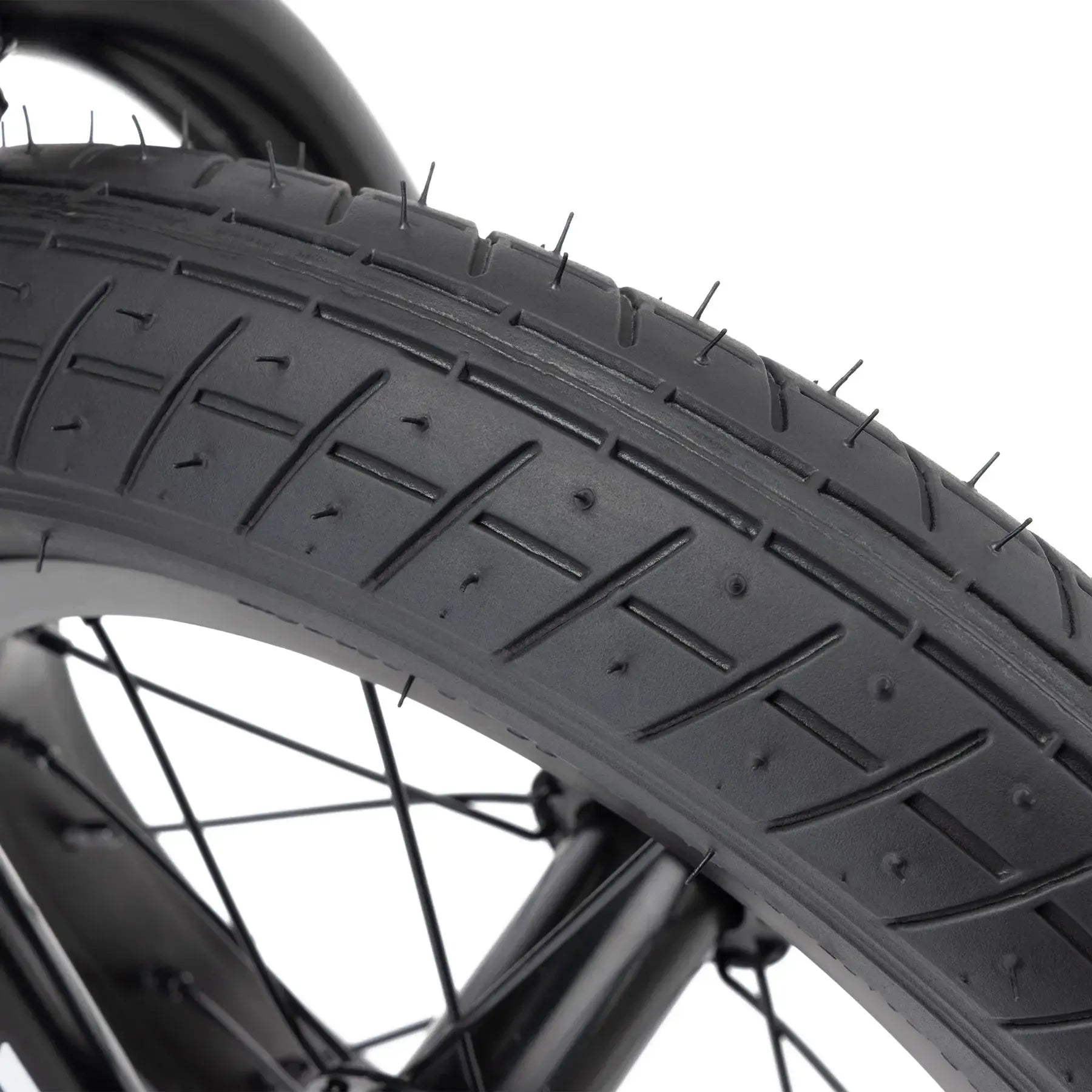 Close-up of a black tire with tread and rubber nubs, plus black spokes—showcasing the Kink Roaster 12 Inch Bike (2026), ideal for kids or anyone picking their first BMX bike.