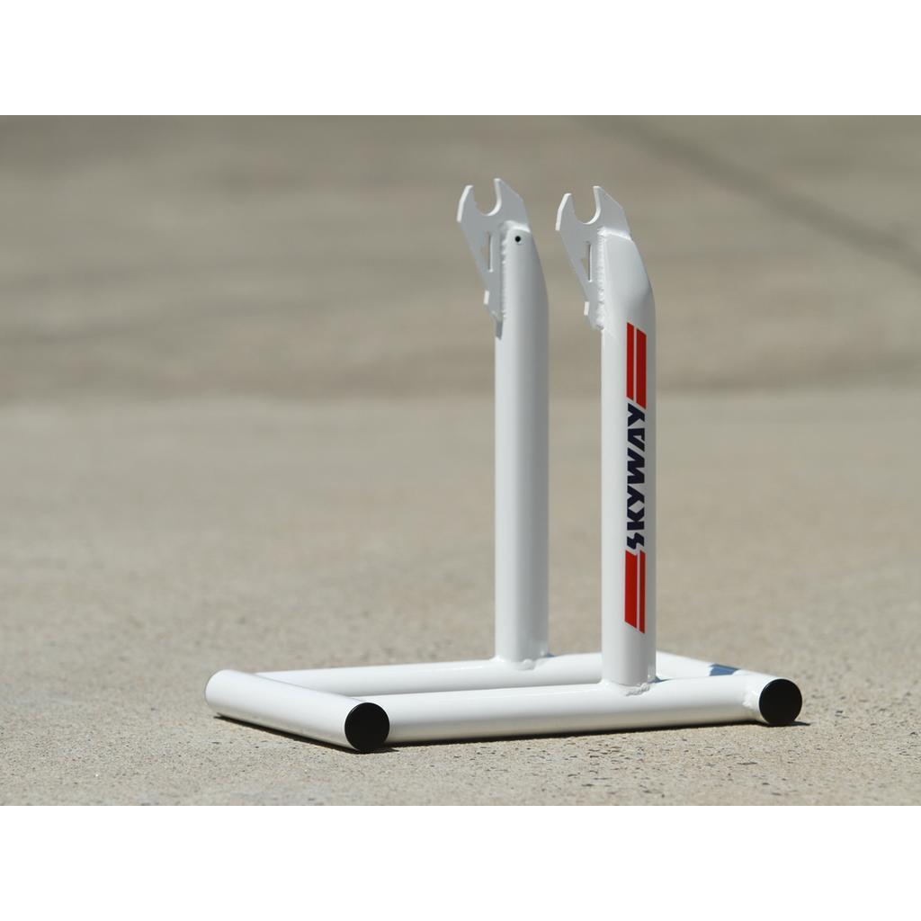 The Skyway Stolz Stand is a white metal BMX display stand with two upright prongs and red/blue "SKYWAY" branding, perfect for showcasing your TA Replica bike on any concrete surface.