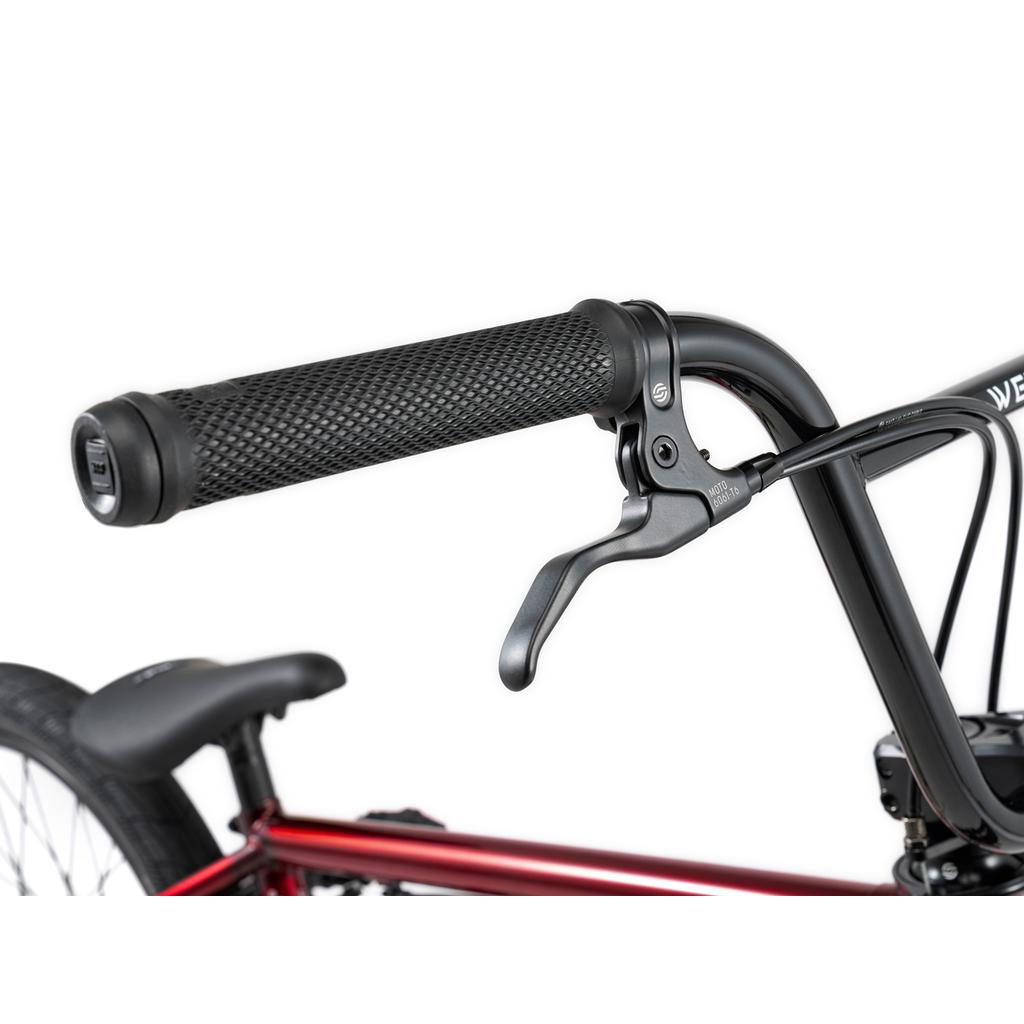 Close-up of the Wethepeople Versus 20 Inch Bike’s handlebar with textured rubber grip, brake lever, and parts of the frame and rear wheel—ideal for skatepark BMX enthusiasts.