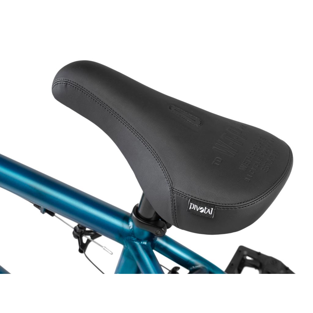 Close-up of a black bicycle seat with visible stitching and a "PIVOTAL" tag, mounted on the Wethepeople Arcade 20 Inch Bike's blue frame. Salt Valon Rims add quality touches to this standout mid-tier BMX model.