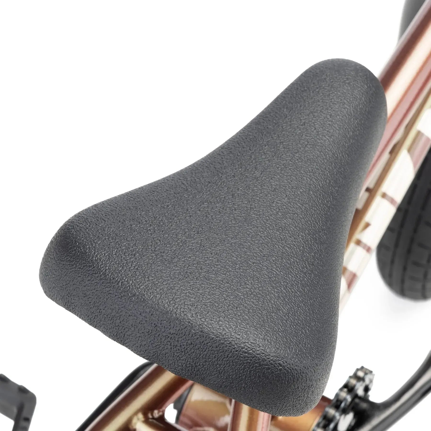 Close-up view of the Kink Roaster 12 Inch Bike (2026) shows its black textured seat on a metallic frame, with pedals and rear wheel visible—perfect as a first BMX bike for kids.