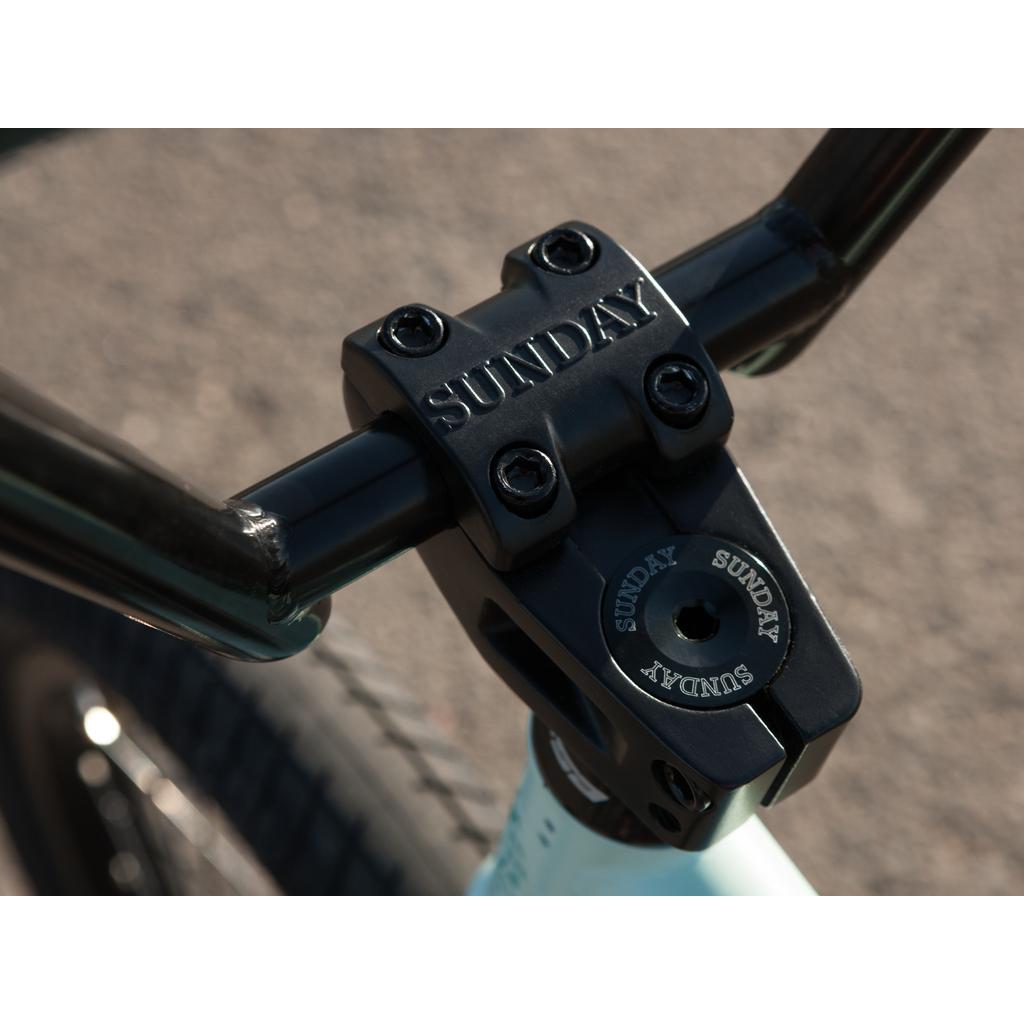 Close-up of the black handlebar and stem on the Sunday EX Julian Arteaga 20 Inch Bike, featuring "Sunday" engraved branding and a 100% chromoly frame.