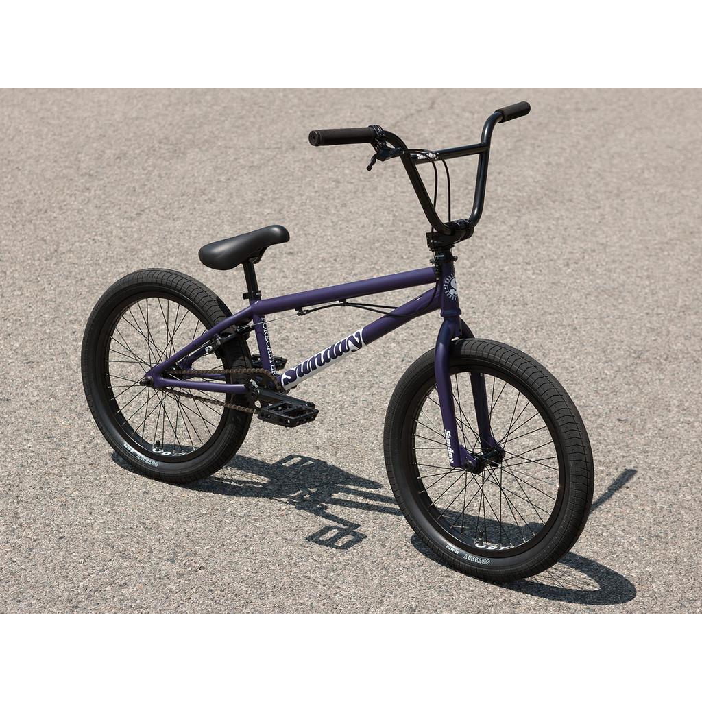 A Sunday Forecaster Maca Grasset 20 Inch Bike in purple with a gyro system, plus black handlebars, seat, and tires, is parked on asphalt.