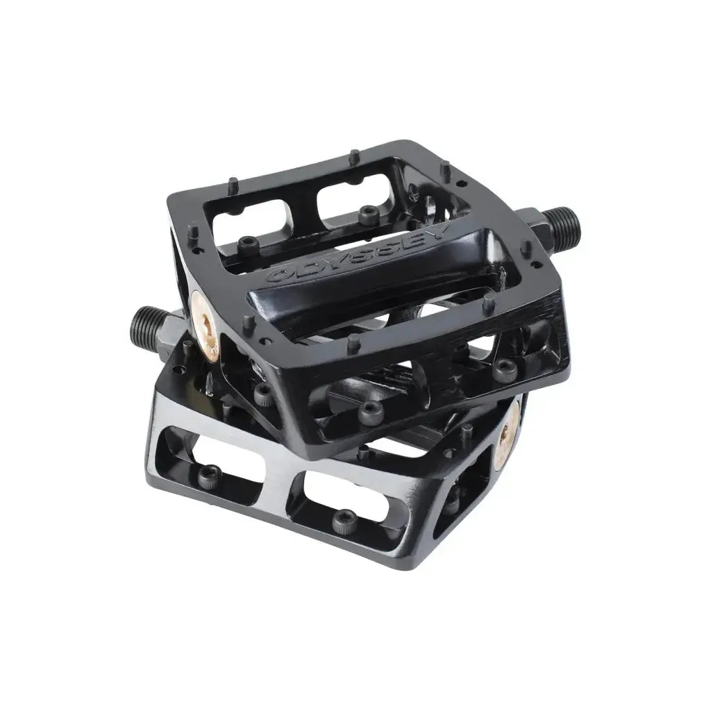 A pair of black Odyssey Trailmix Sealed Pedals with a rectangular, open-frame platform and grip pins are stacked neatly. They feature sealed bearing construction for smooth performance.