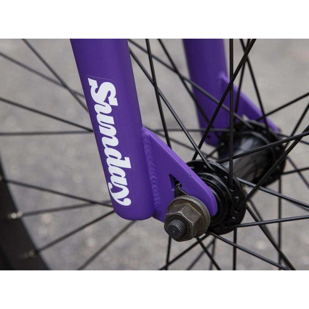 Close-up of the Sunday Forecaster 20 Inch Bike wheel, featuring black spokes and a purple fork with "Sunday" in white text, built with quality Odyssey parts.