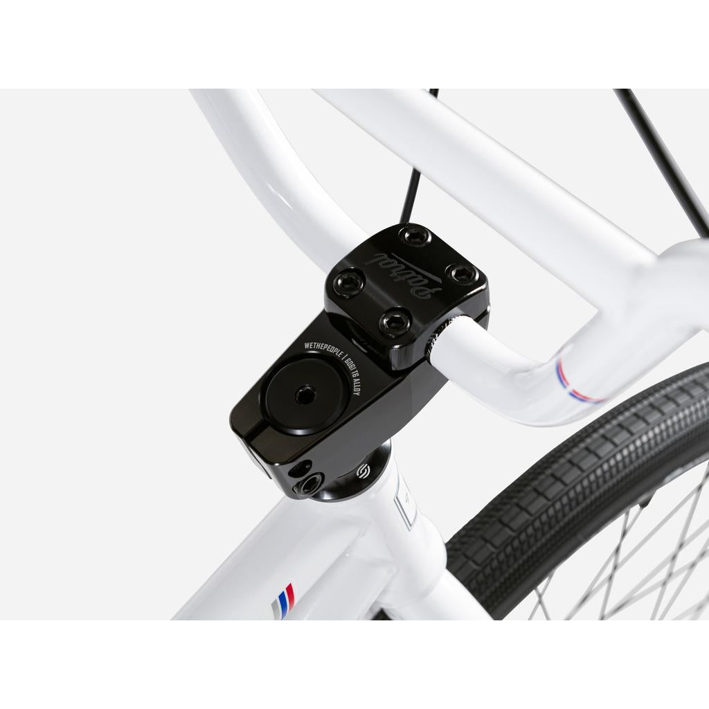 Close-up of the Wethepeople Atlas 24 Inch Bike’s white handlebars and stem with black hardware, focusing on the stem clamp and part of the 24 inch wheels.