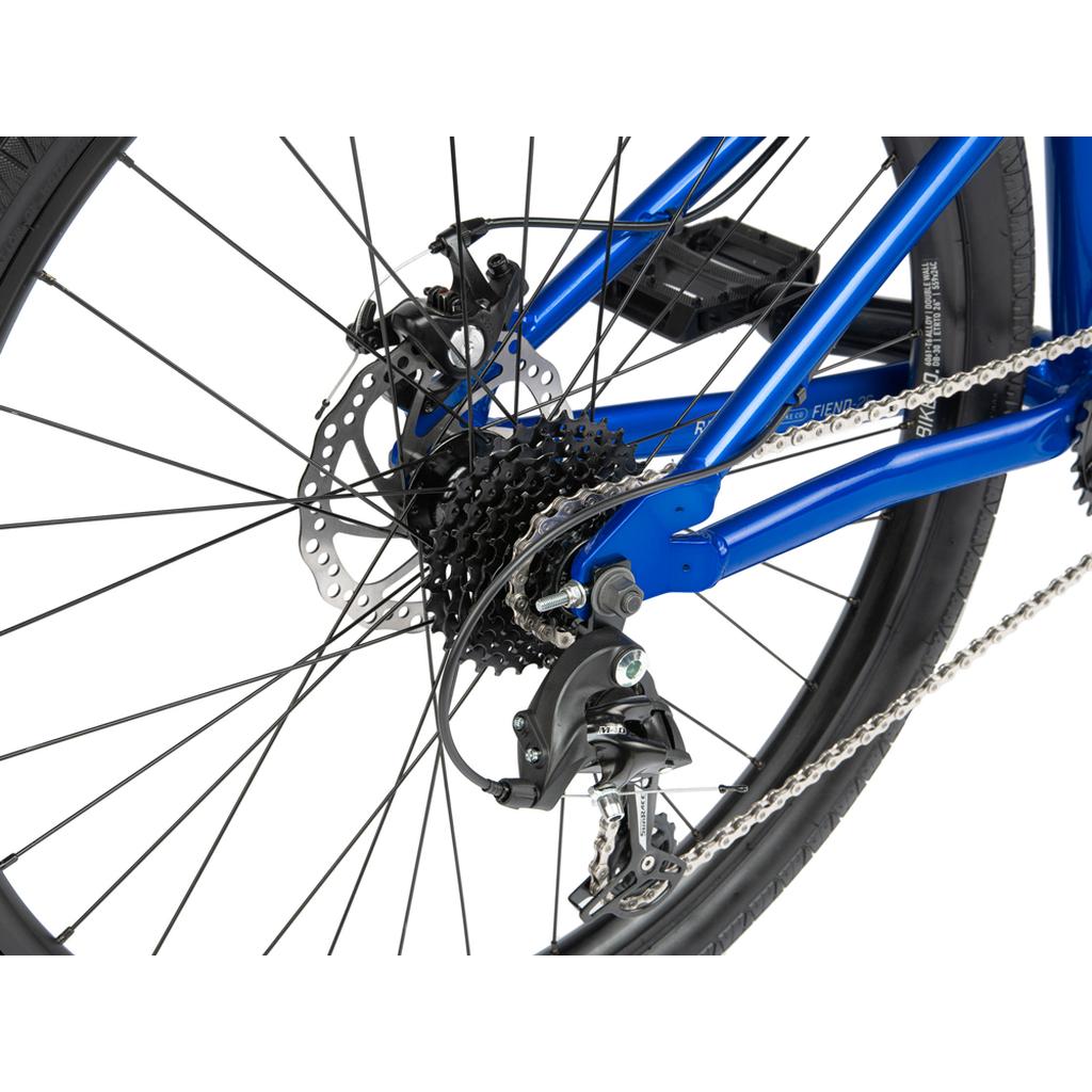 Close-up of the Radio Fiend 26 Inch Bike's blue rear wheel, featuring gears, derailleur, chain, disc brake rotor, and part of its 6061-T6 alloy frame.