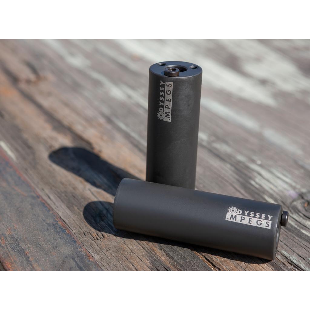 Two Odyssey MPEG Pegs Pair rest on a weathered wooden surface, one upright and the other lying down—ideal chromoly pegs for any BMX setup.