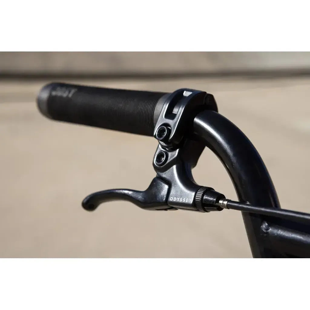 Close-up of a black handlebar grip and brake lever branded "Odyssey" on the Sunday Soundwave Special Bike (2025), highlighting quality Odyssey parts outdoors in daylight.