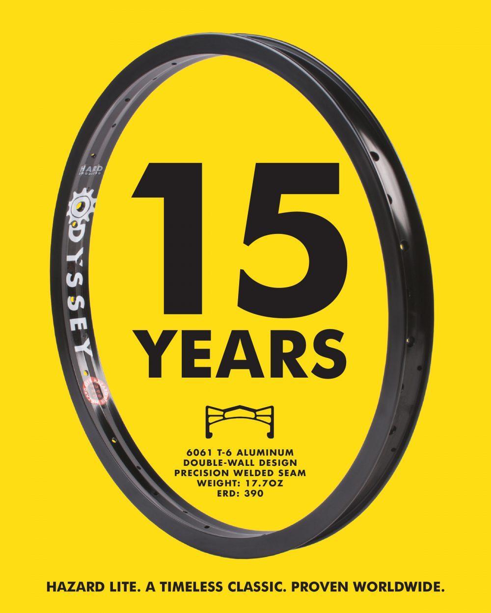 A black Odyssey Hazard Lite Rim, a strong and lightweight BMX rim, is shown on a yellow background with bold "15 YEARS" text. Key specs and the tagline are also featured.
