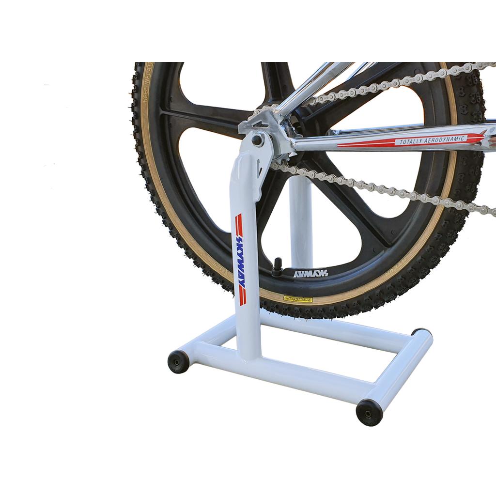 A close-up of a bike's rear wheel on a Skyway Stolz Stand, featuring black wheels, part of the frame, and the chain.