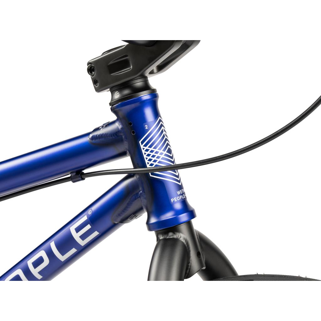 Close-up of the Wethepeople CRS FC 20 Inch Bike's blue frame featuring a white geometric logo and black front brake cable near the handlebars and front wheel.