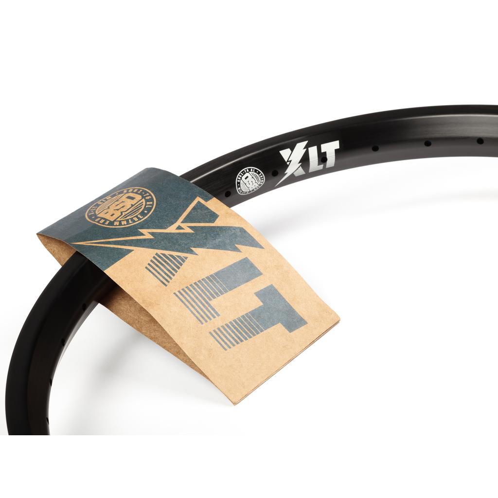 The BSD XLT Rim is a lightweight black BMX rim featuring the "XLT" logo and stickers, with a brown and blue paper tag labeled "XLT" attached.