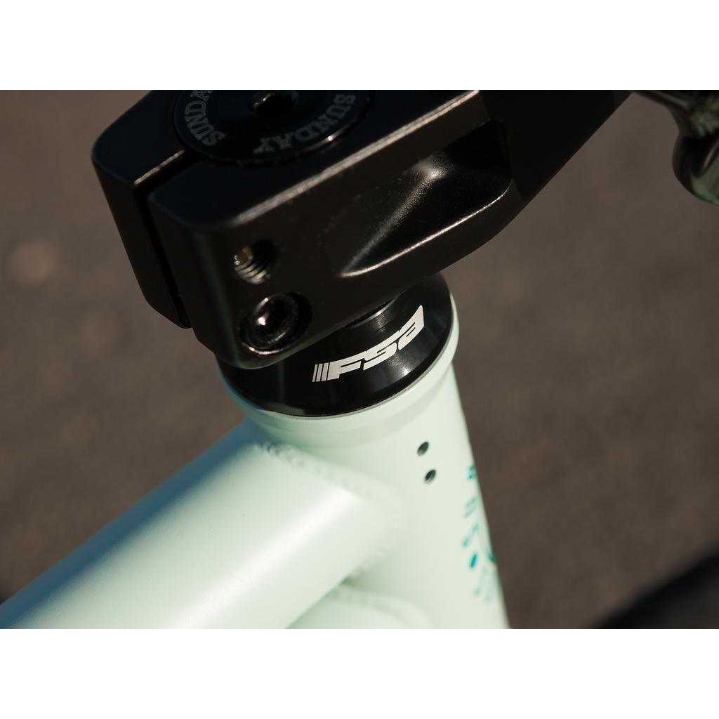 Close-up of the Sunday EX Julian Arteaga 20 Inch Bike's head tube area, showing its FSA headset and part of the black handlebar stem, with a blurred outdoor background.