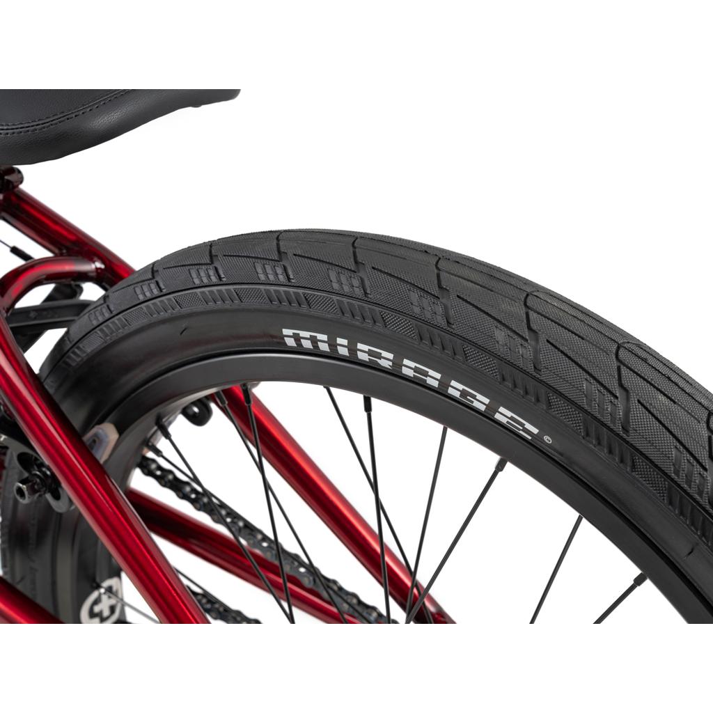 Close-up of a black Mirage tire on the rear wheel of a red Wethepeople Versus 20 Inch Bike, showcasing its tread—ideal for skatepark BMX enthusiasts.