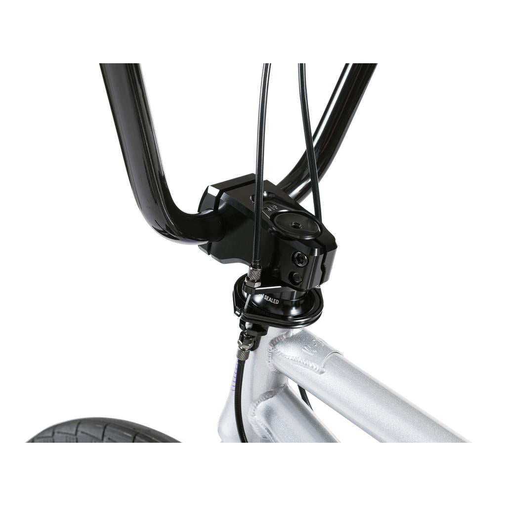 Close-up of the Wethepeople Versus 20 Inch Bike's handlebar and stem assembly, with visible brake cables and part of the front wheel.