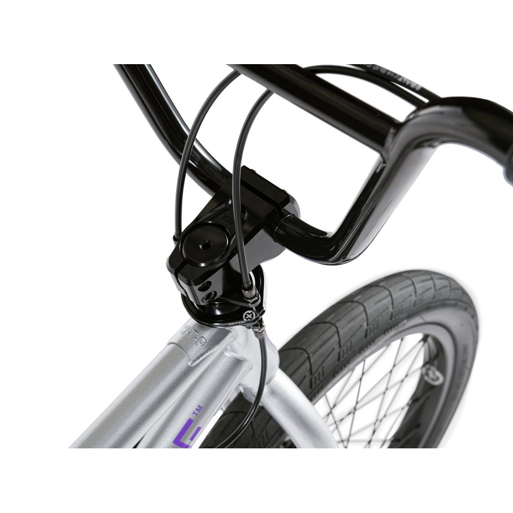 Close-up of the Wethepeople Versus 20 Inch Bike's black handlebars, stem, and front tire with visible brake cables and part of its durable silver frame—designed for tough skatepark sessions.