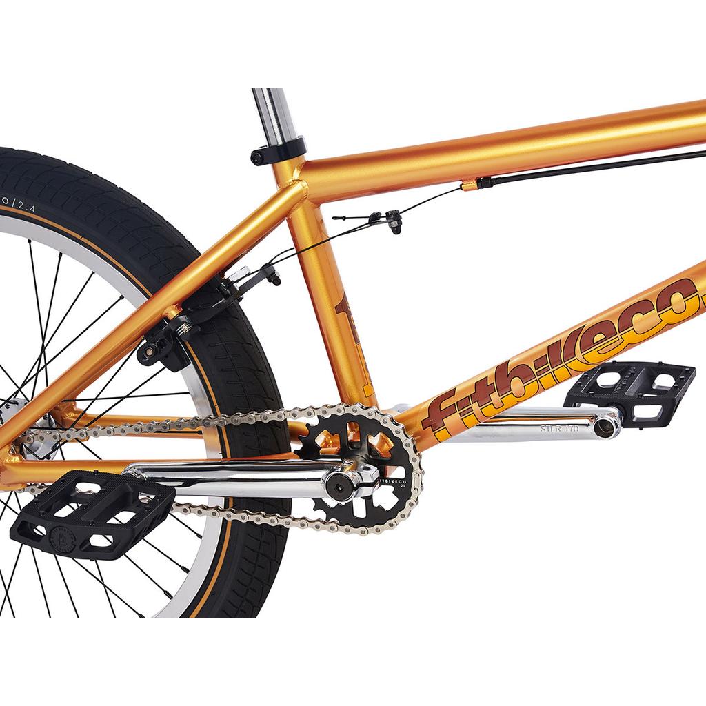 Close-up view of the crankset, pedals, chain, and rear wheel of a metallic orange Fit Series One 20 Inch Bike (2023) with "fitbikeco" branding on the frame.