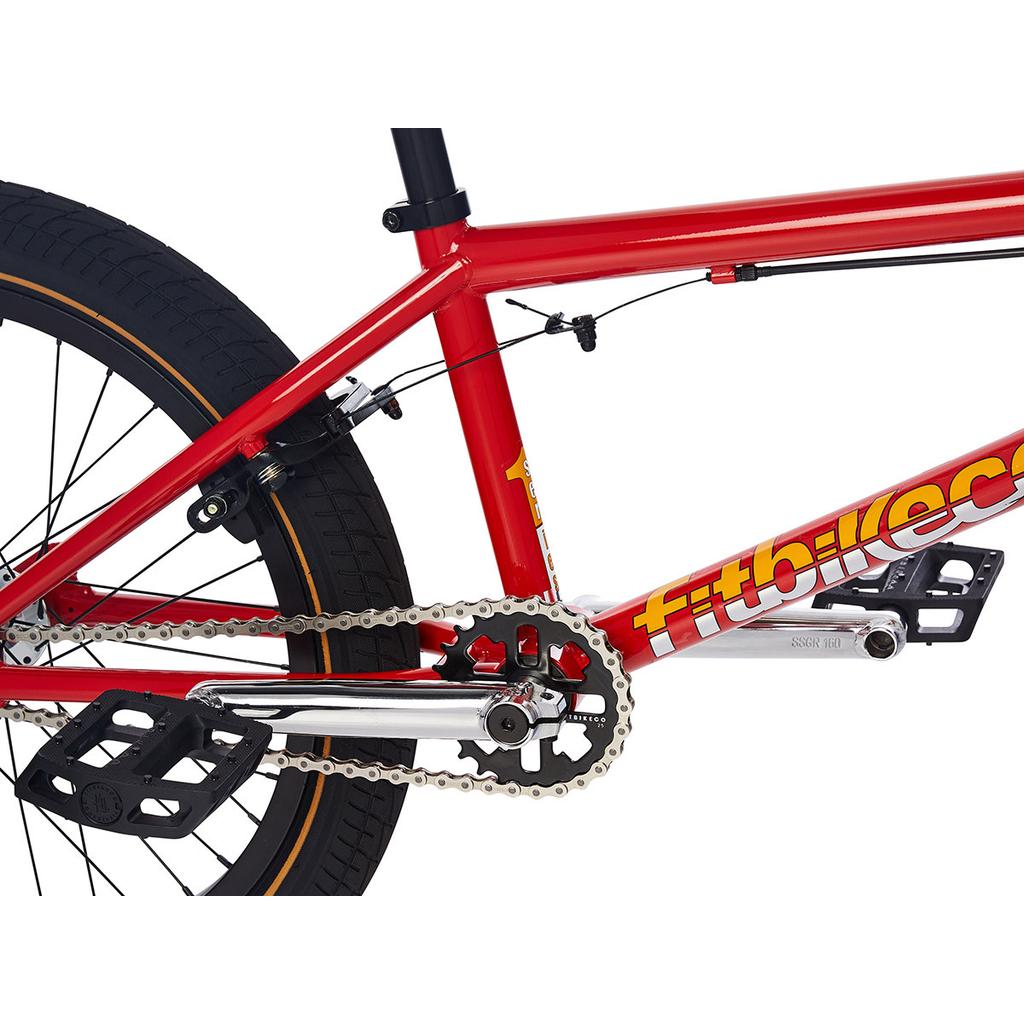 Close-up of the Fit Series One 20 Inch Bike (2023) in red, highlighting its entry-level BMX frame with chain, pedals, crankset, rear brake, and rear wheel featuring visible tire tread and branding.