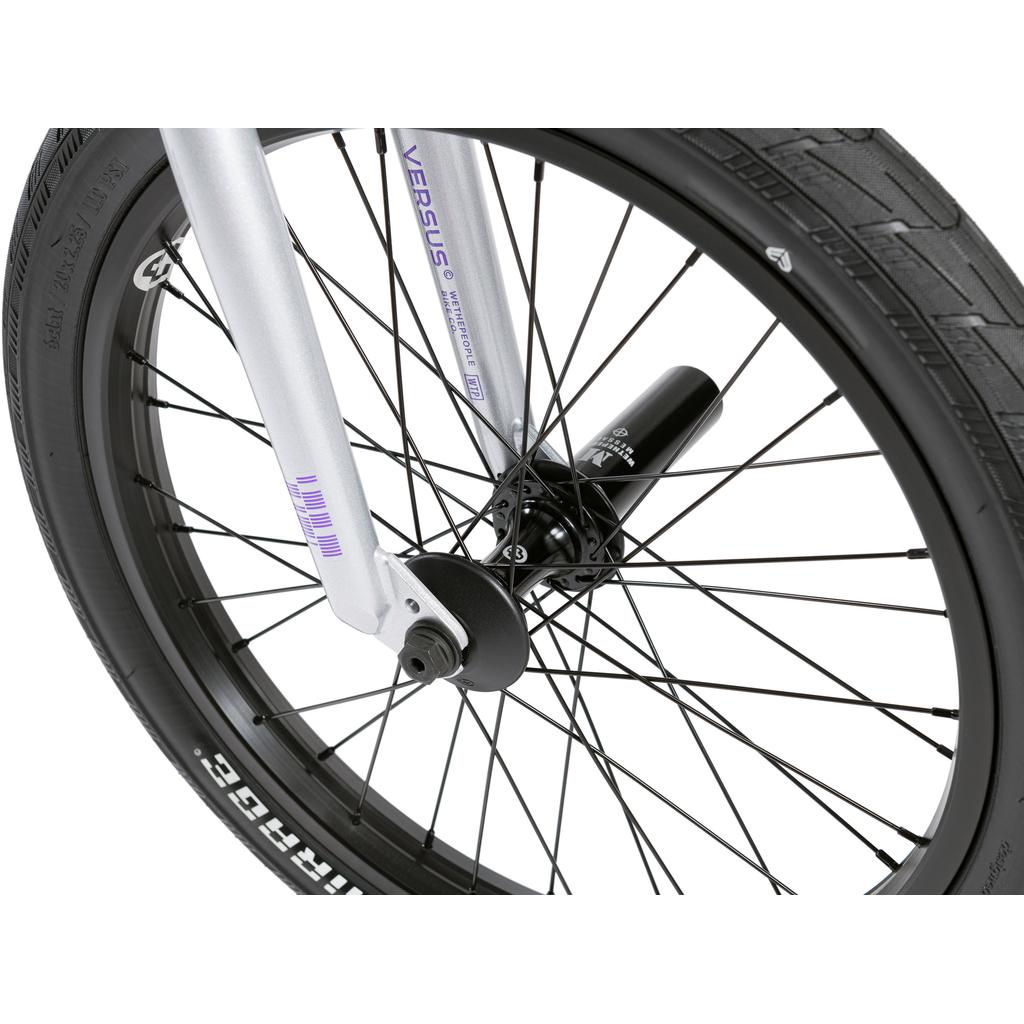 Close-up of a BMX front wheel with black spokes, silver fork, and black tire, showing the hub and axle fastened with a nut—ideal for the Wethepeople Versus 20 Inch Bike at the skatepark.