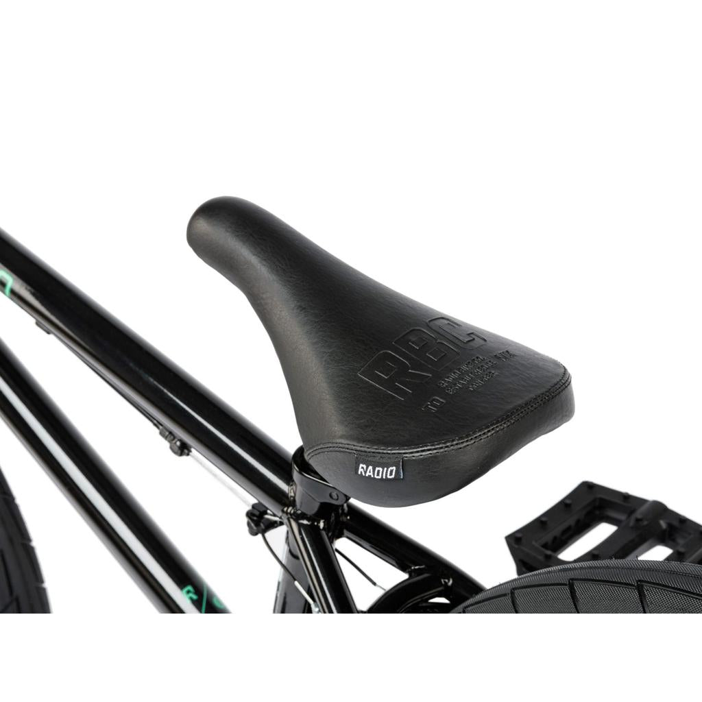 Close-up of a black RBC-embossed bicycle seat attached to the Radio Saiko 20 Inch Bike frame and wheel, photographed against a white background.