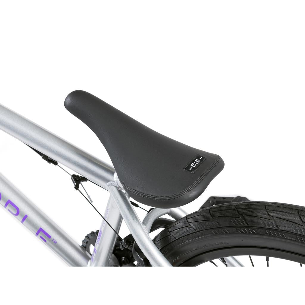 Close-up of a black seat on a silver Wethepeople Versus 20 Inch Bike, showing part of the rear wheel and tire.