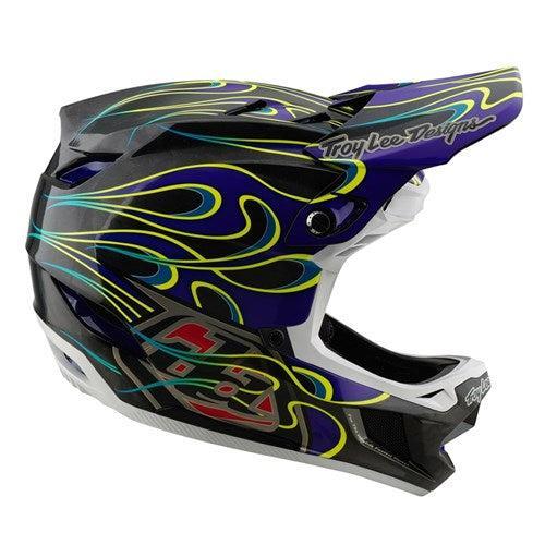 The TLD 25.1 D4 Carbon Helmet (MIPS) in Torched Black/Purple boasts a striking design with yellow flames and "Troy Lee Designs" on the visor, offering cutting-edge safety without compromising style.