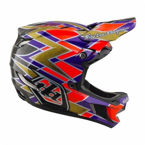 Introducing the TLD 26.2 D4 Carbon Full Face Helmet / MIPS Flush Violet—a downhill mountain bike helmet featuring a black base with gold, red, and purple geometric patterns. With “Troy Lee Designs” proudly displayed on the visor and advanced MIPS protection integrated for enhanced trail safety, this helmet delivers both standout style and top-tier performance.