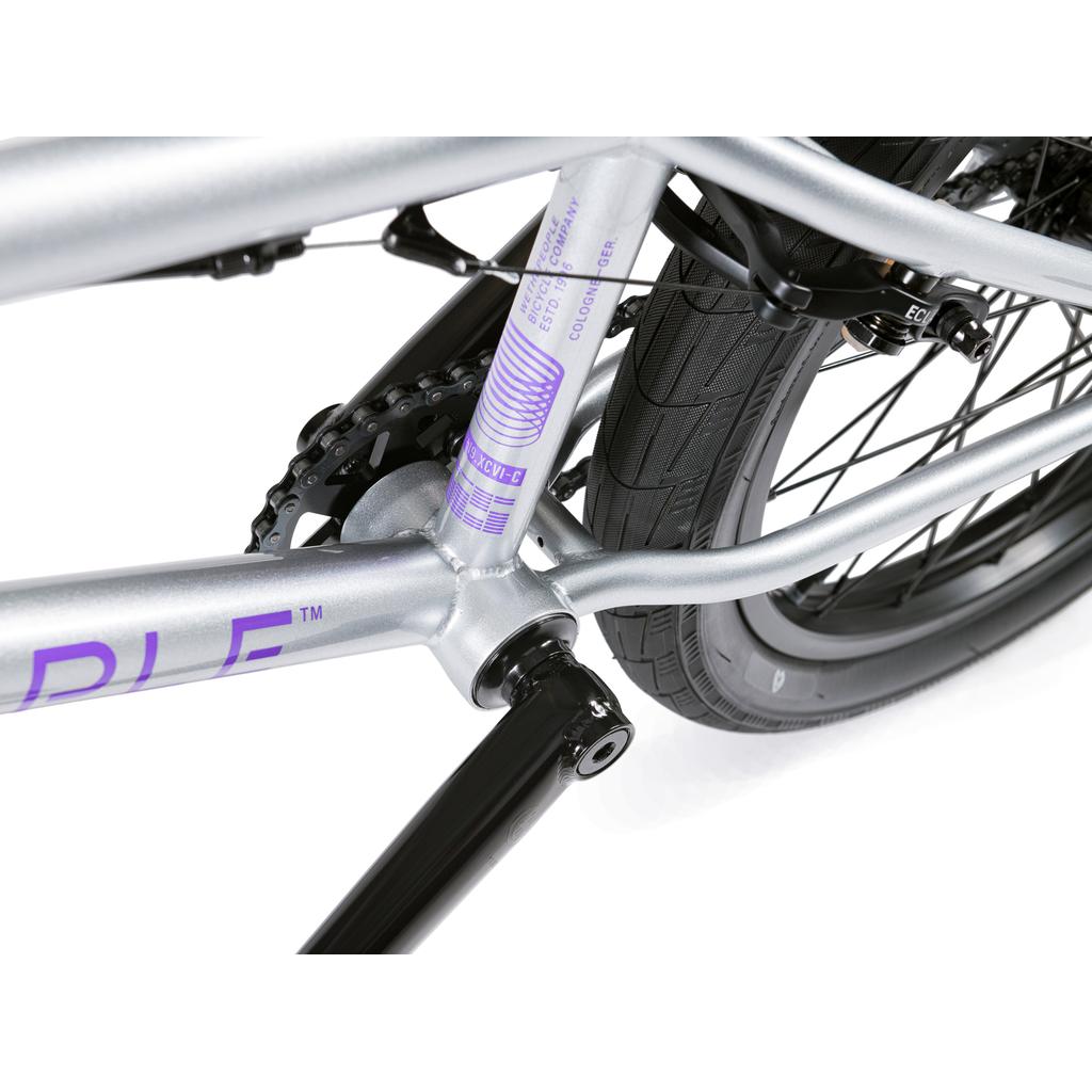 Close-up view of the Wethepeople Versus 20 Inch Bike's rear frame, chain, tire, and crank arm, showcasing its silver and purple color scheme.