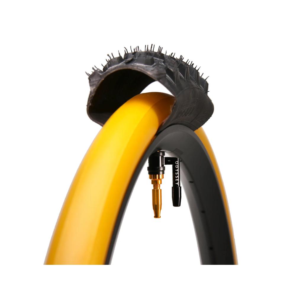 Close-up of the Odyssey OPTIS Insert With Valve P/V Tube (27.5 Inch) installed, showing the yellow liner beneath a cutaway black tire and the valve stem on the rim for enhanced tire protection.