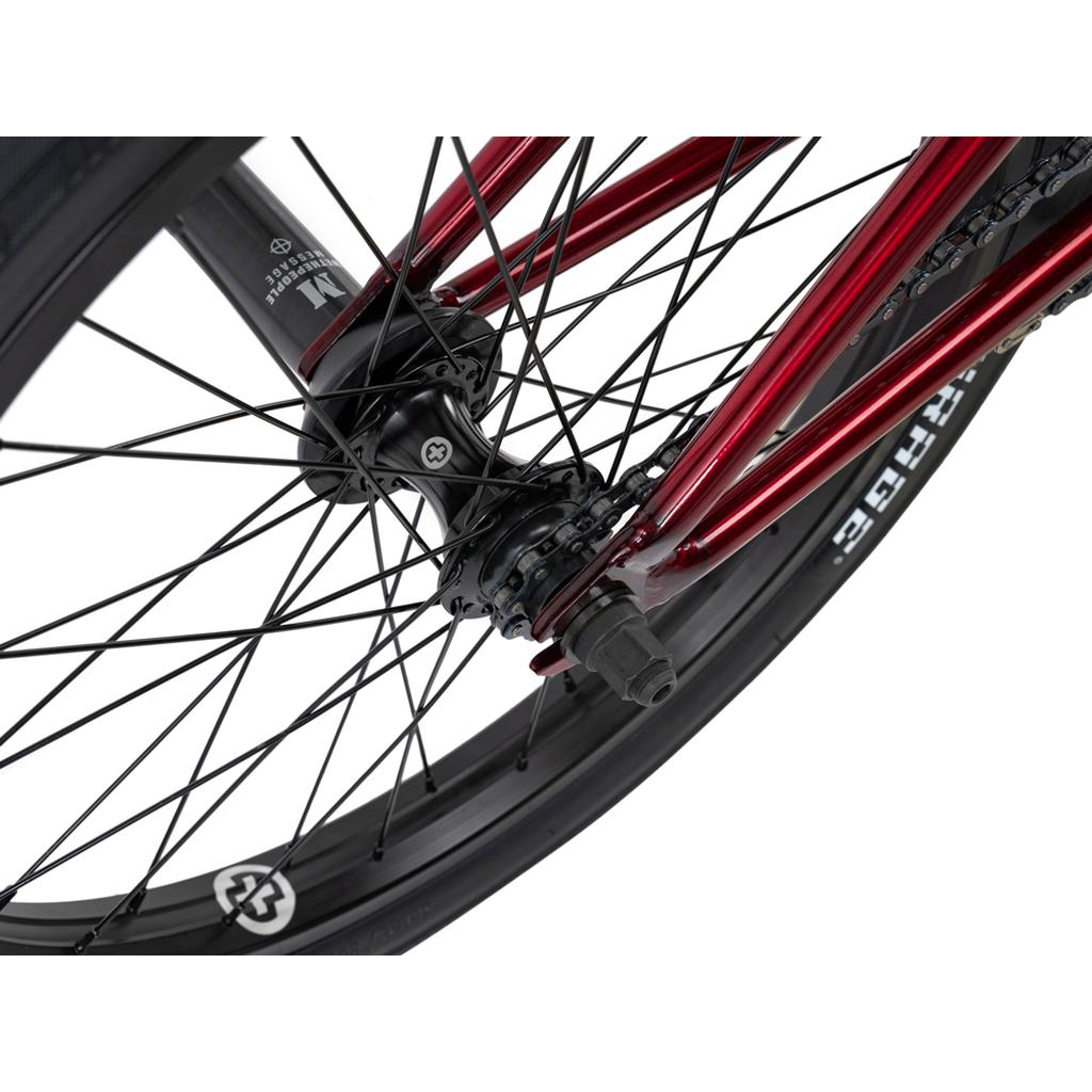 Close-up of the Wethepeople Versus 20 Inch Bike’s rear wheel hub, spokes, and axle, showing its red frame and black tire—ideal for skatepark rides.