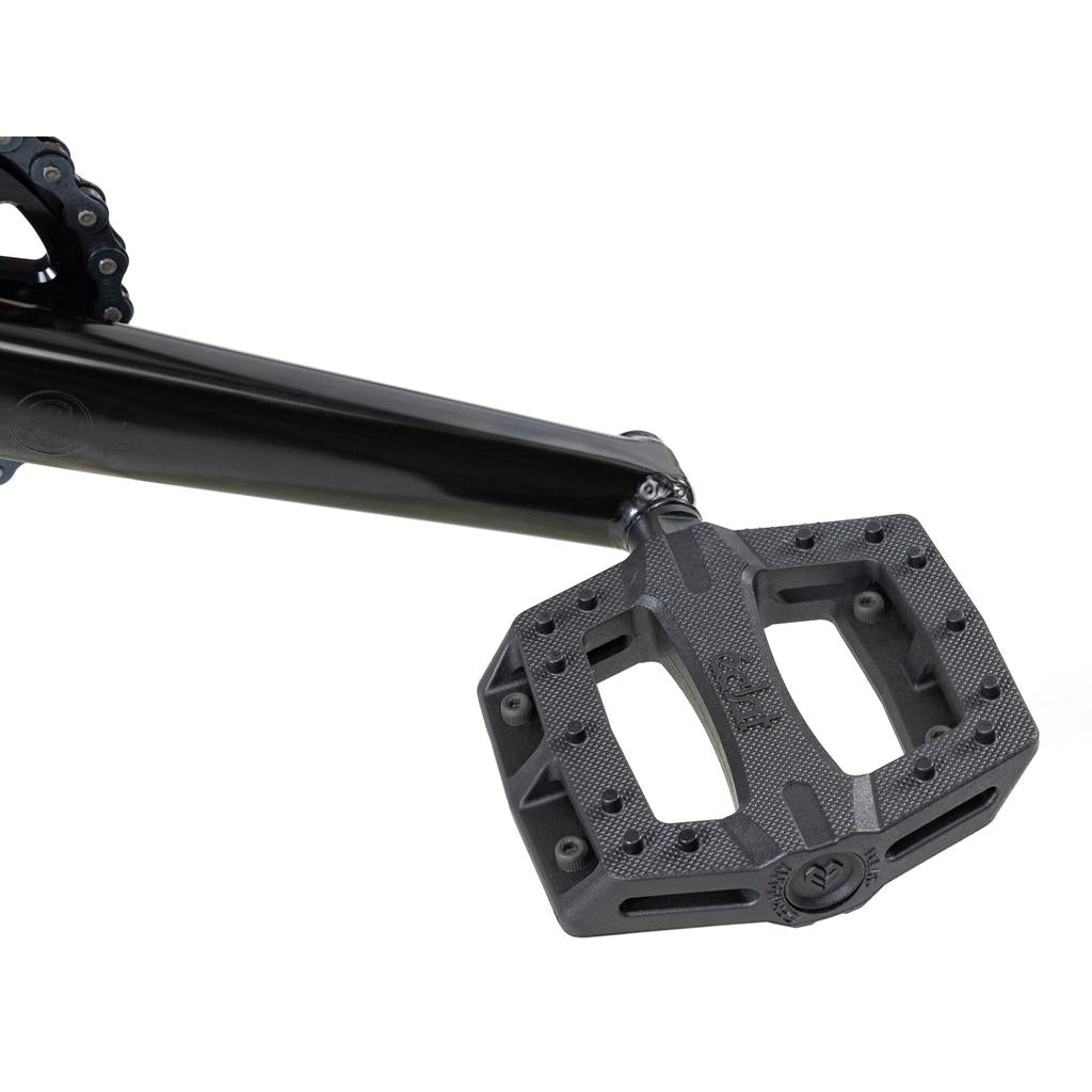 Close-up of a Wethepeople Versus 20 Inch Bike crank arm attached to a flat, rectangular pedal with a textured surface and pin studs for added grip.