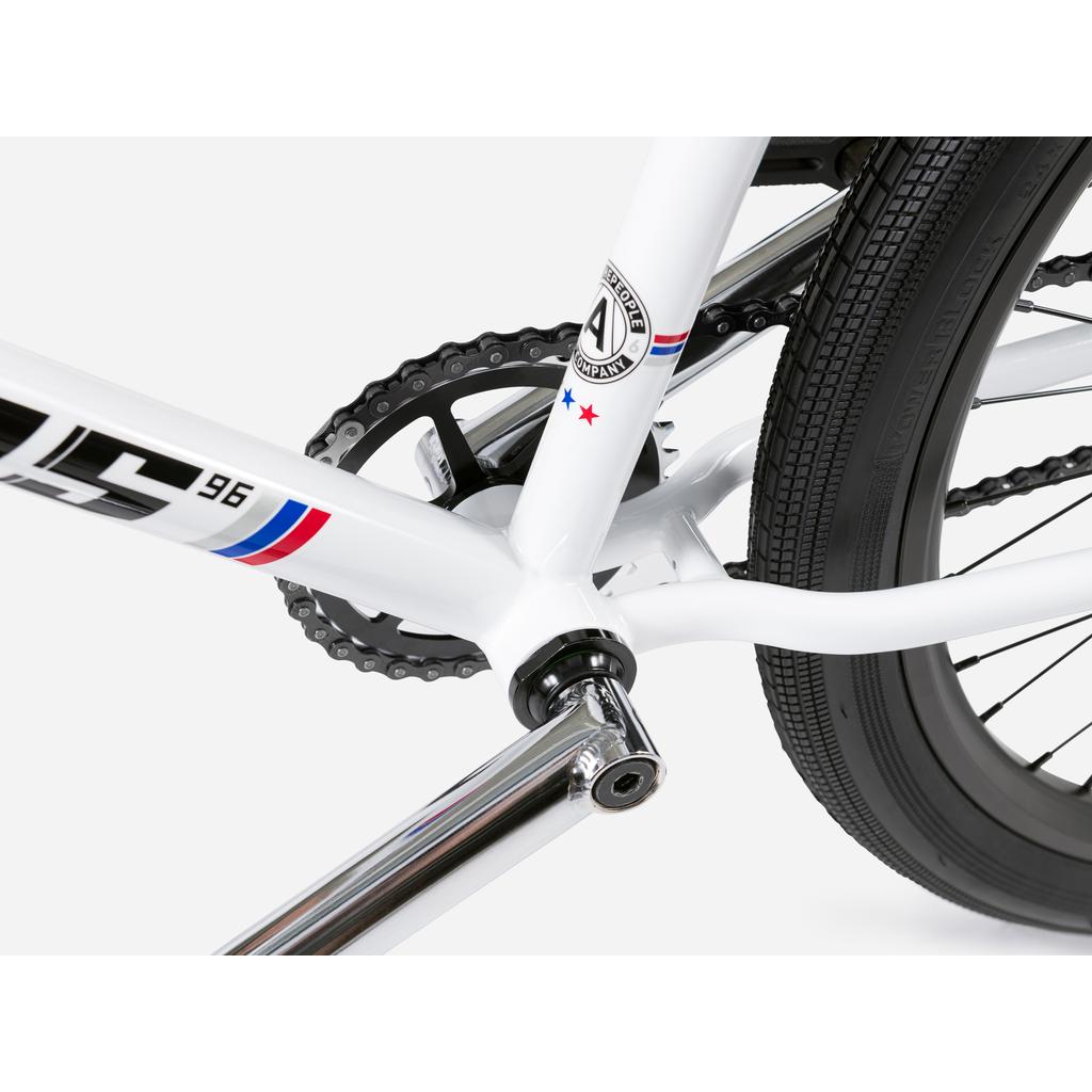 Close-up of the Wethepeople Atlas 24 Inch Bike’s crankset, chain, wheels, and frame, highlighting its clean components and detailed logo near the bottom bracket.