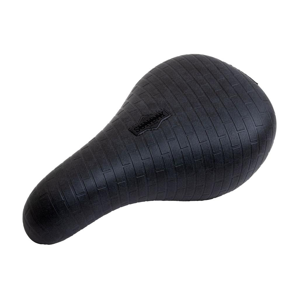 The Sunday Pivotal Seat (Brett Silva Signature) is a black custom BMX seat featuring a brick-textured pattern and a small central Sunday logo, inspired by Brett Silva.