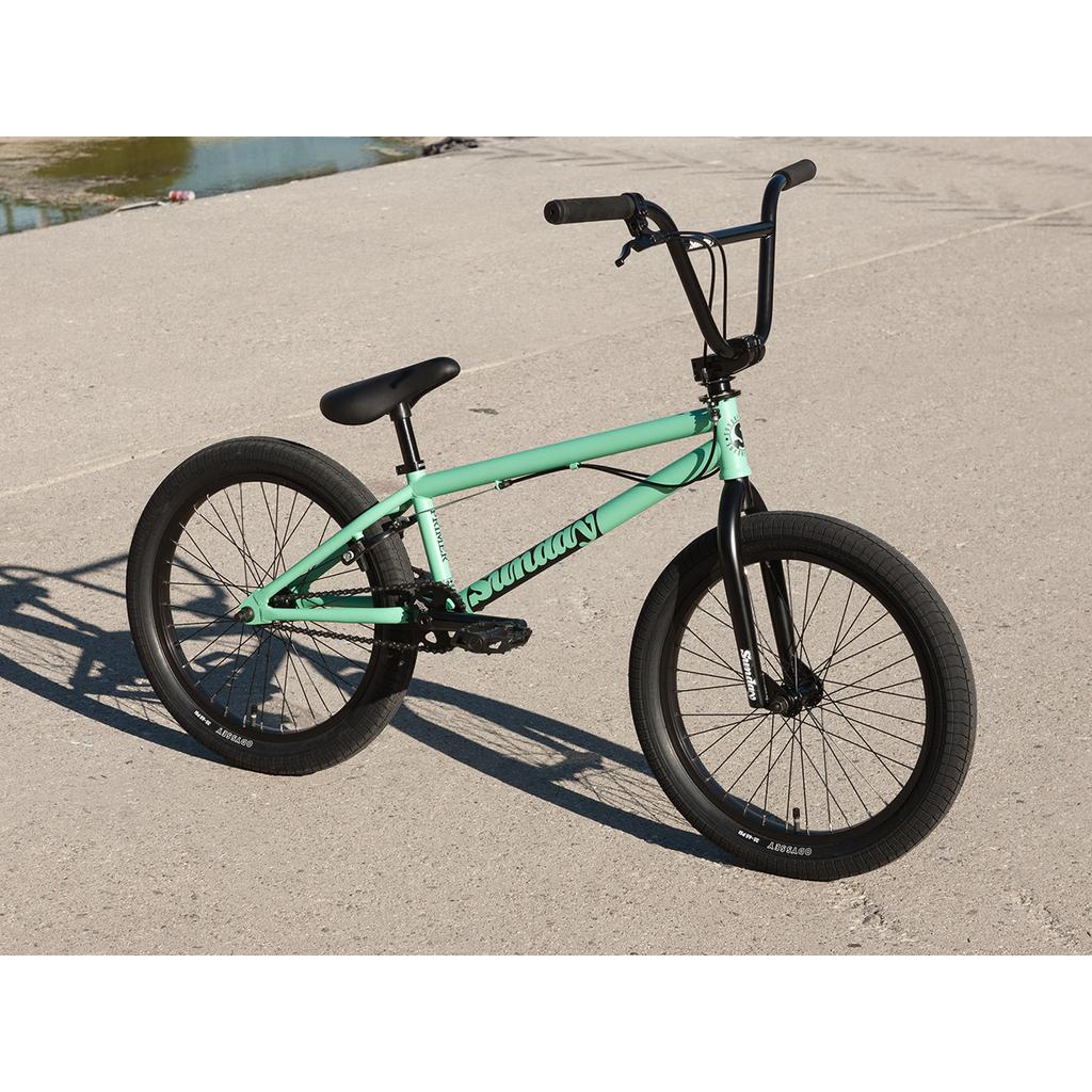 A Sunday Primer Park 20 Inch Bike in mint green, with black handlebars, seat, and tires and a gyro setup, is parked on concrete in daylight.