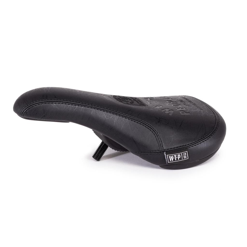 The Wethepeople Team Pivotal Slim Seat is a lightweight black BMX seat with a textured surface, visible stitching, bolt attachment underneath, and a white “WTP” logo on the lower right side. Features a pivotal design inspired by pro riders.