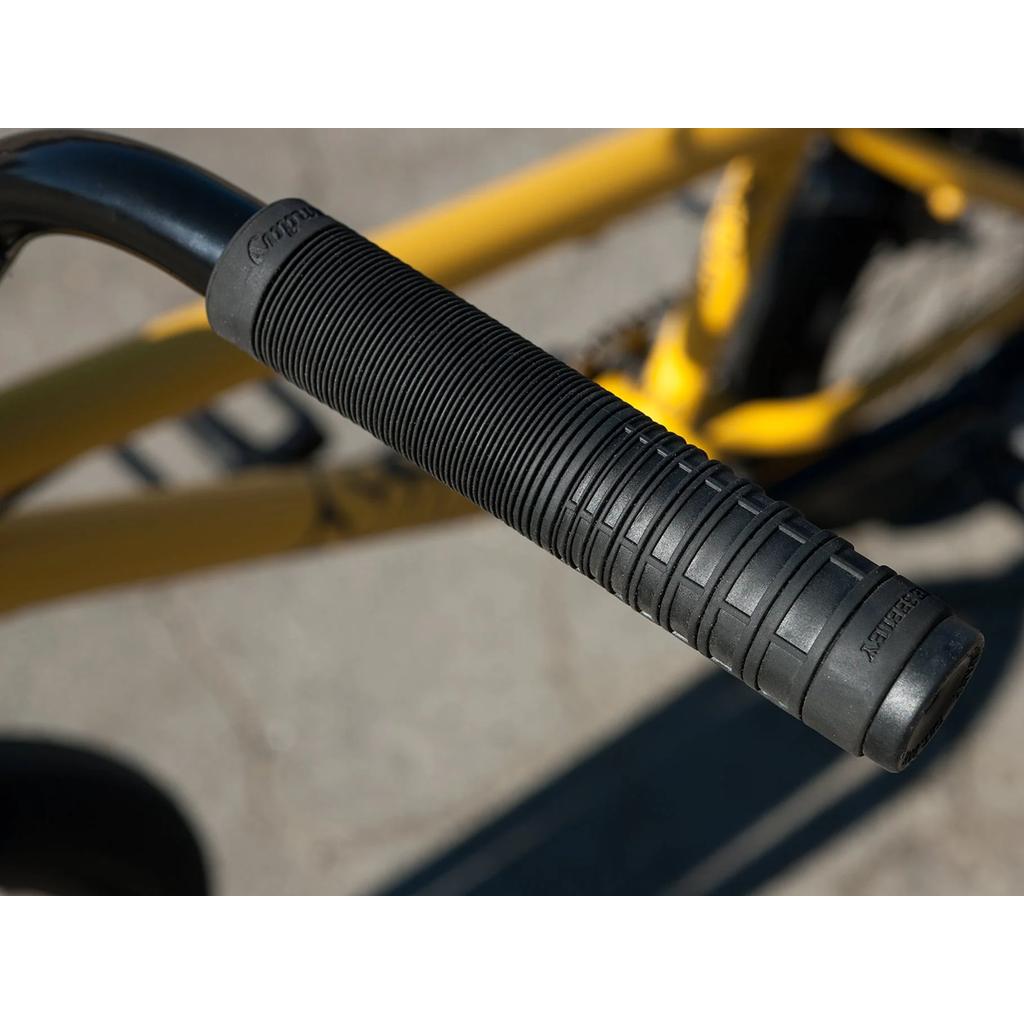 Close-up of a black rubber handlebar grip with textured ridges on the Sunday Scout 20 Inch Bike, featuring part of its yellow chromoly frame in the background.