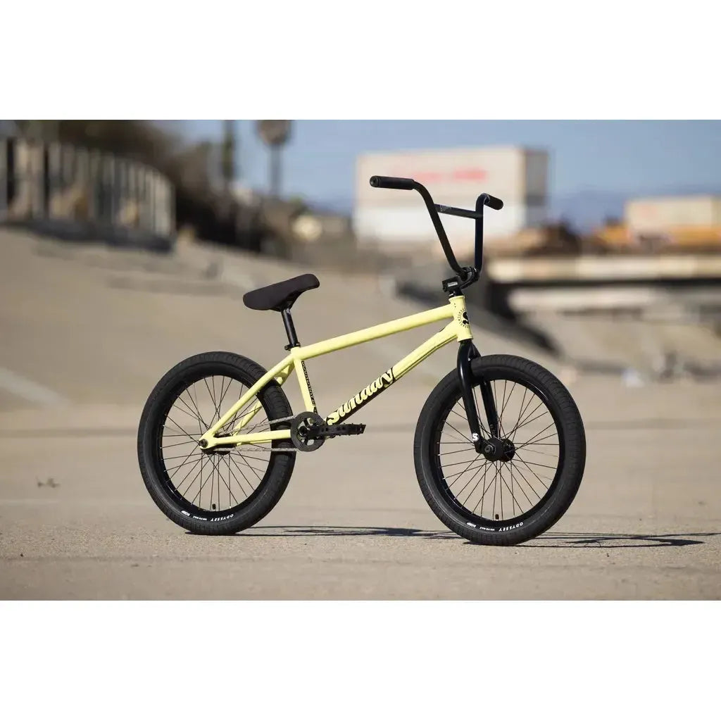 A yellow Sunday Soundwave Special Bike (2025) with black handlebars, seat, and tires—featuring Odyssey parts and a 41-Thermal Lifetime Warranty—is parked on a concrete surface outdoors.