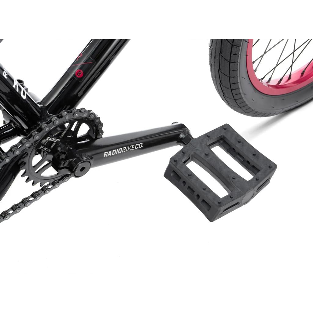 Close-up of the black crankset, pedal, chainring, and rear wheel with a pink rim and Salt Tracer Tyres on the Radio Saiko 18 Inch Bike, shown against a white background.