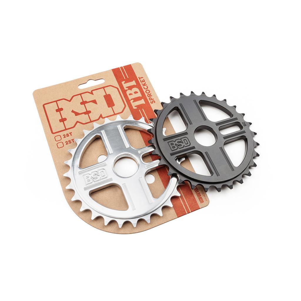 Two BSD TBT Sprockets in silver and black, crafted from 7075 aluminium, are displayed on branded packaging. Available in 25T and 28T sizes, the BSD TBT Sprocket is ideal for upgrading your BMX setup.