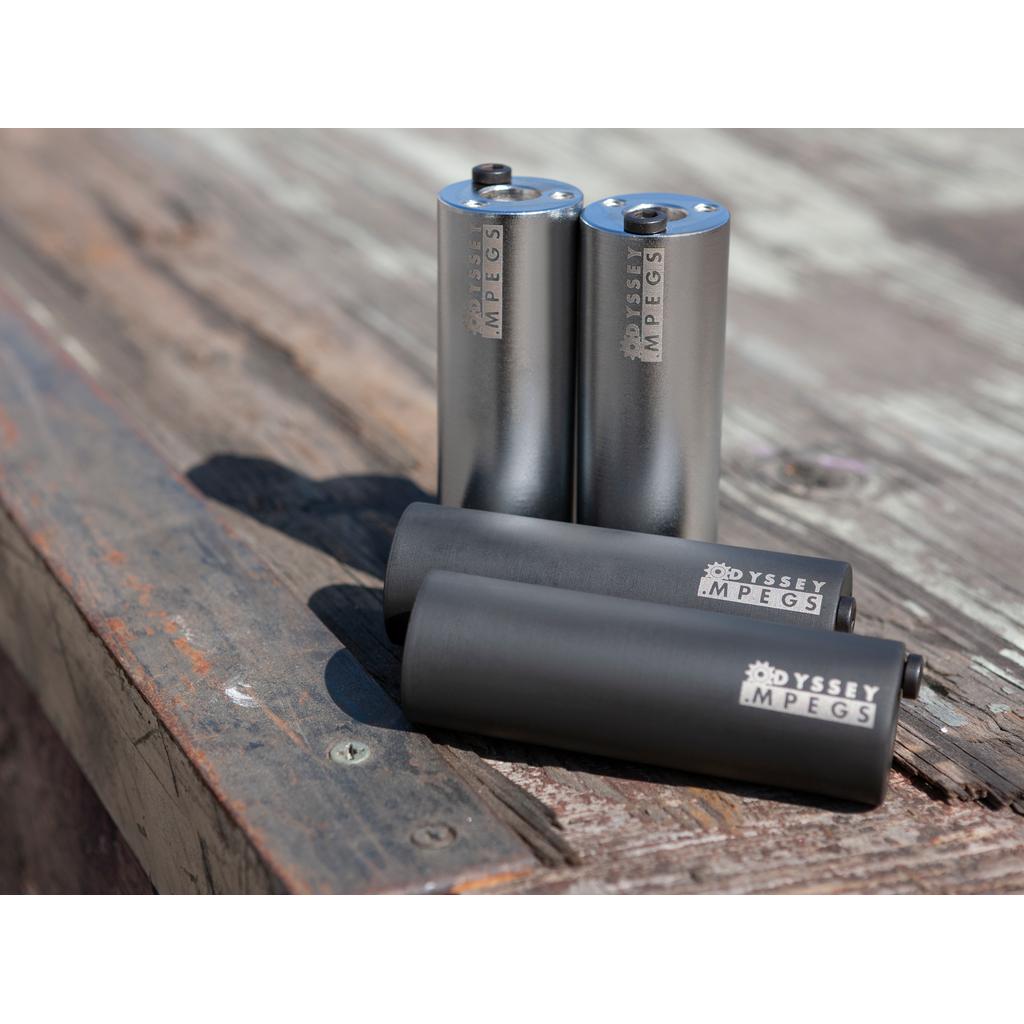 Two pairs of Odyssey MPEG Pegs are displayed on a weathered wooden surface—two standing upright and two lying down.