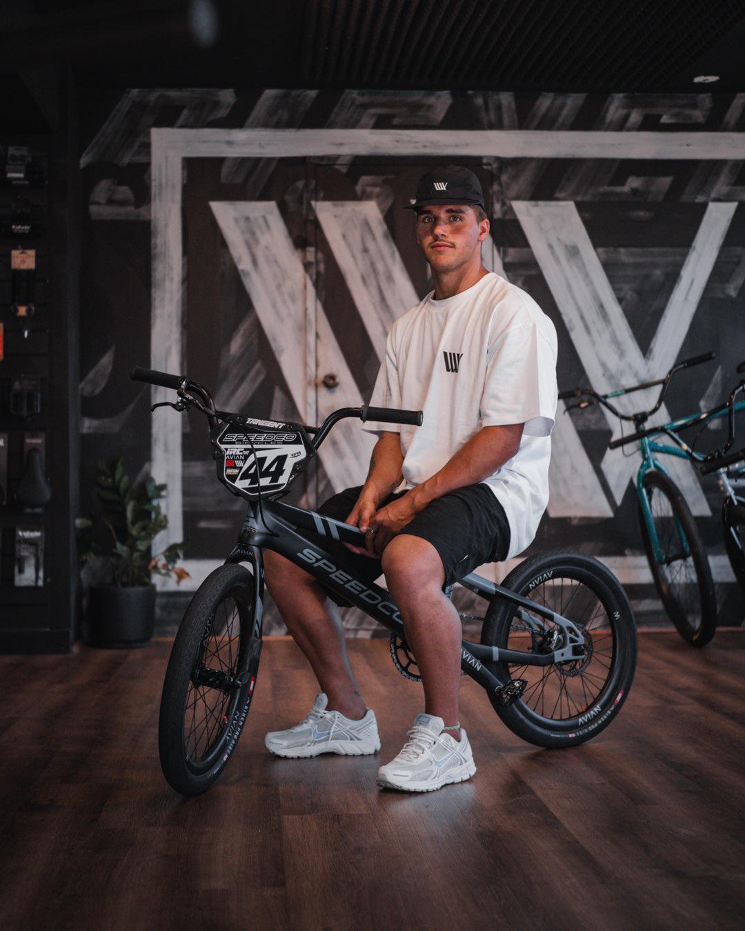 A man sitting on a LUXBMX Izaac X Rico Tee in a store.