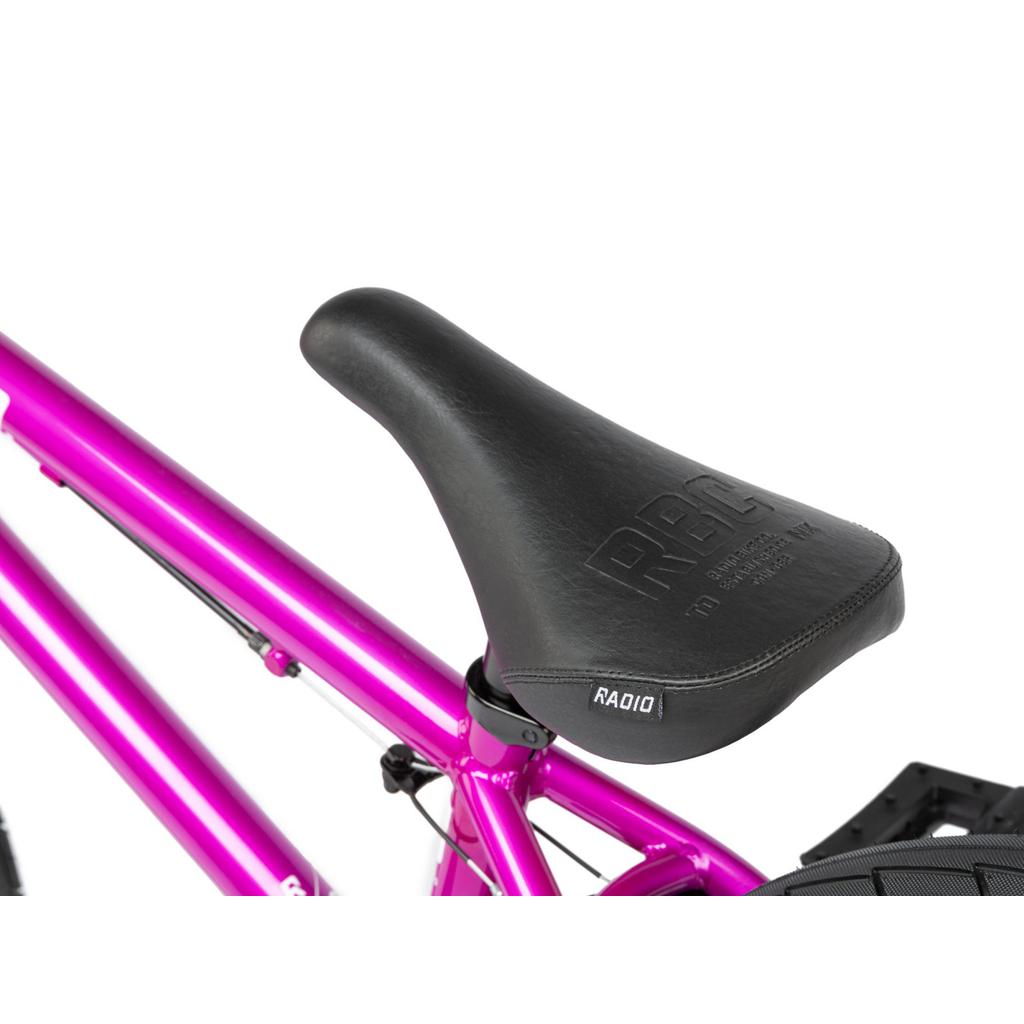 Close-up of a black bicycle seat attached to the metallic pink frame of a Radio Saiko 20 Inch Bike, with "Radio" branding visible on the seat.
