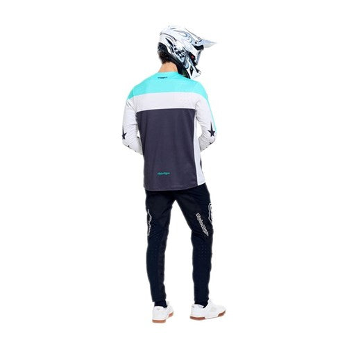 A person stands facing away from the camera against a white background, wearing a motocross helmet, long-sleeve jersey, and TLD 26.1 Sprint Pro Pants / Mono Black made with durable 4-way stretch fabric.