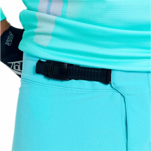 Close-up of a person wearing TLD 26.1 Sprint Pro Pants in Mono Real Teal, made with durable 4-way stretch fabric. A black belt and a partially visible gloved hand at the waist are shown.